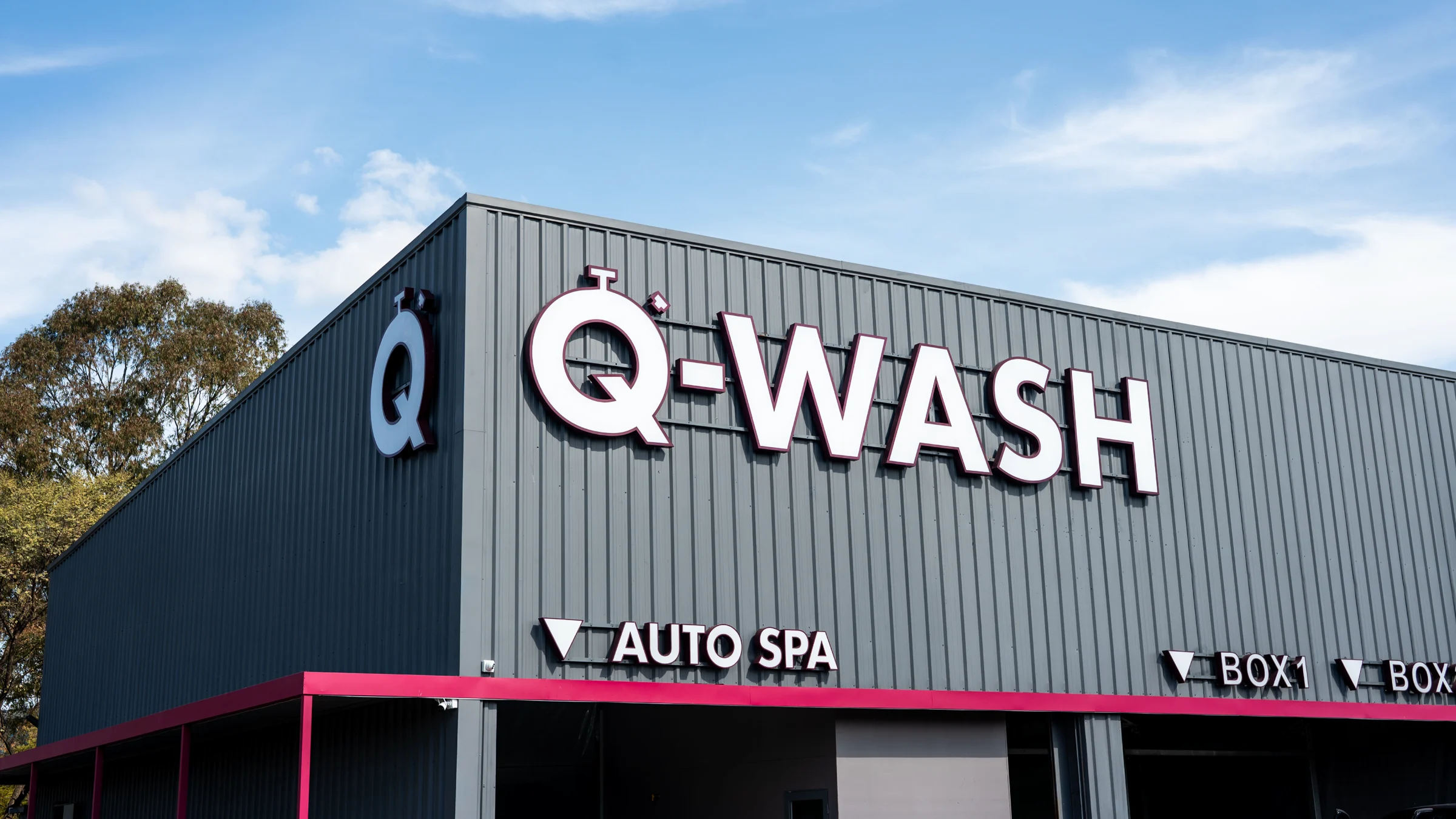 Fachada de Q-WASH con el cartel de Auto Spa y los boxes de lavado